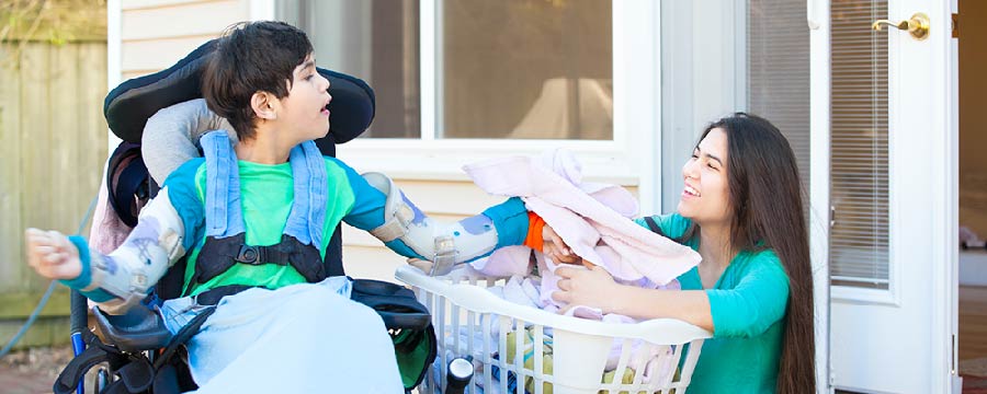 young boy with cerebral palsy in wheelchair assisting his mom with laundry in front yard